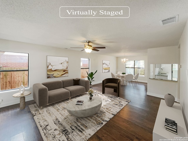 living room with ceiling fan with notable chandelier, a textured ceiling, and dark wood-type flooring