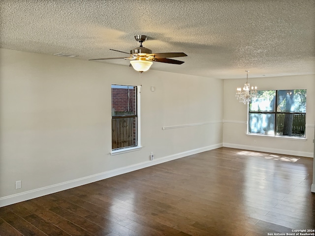 empty room with a textured ceiling, ceiling fan with notable chandelier, and dark hardwood / wood-style floors