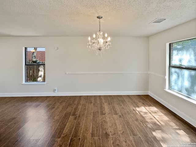 empty room featuring a textured ceiling, plenty of natural light, dark hardwood / wood-style flooring, and a chandelier