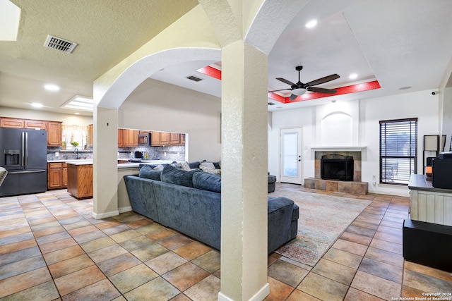 tiled living room featuring a textured ceiling, a tile fireplace, sink, a raised ceiling, and ceiling fan