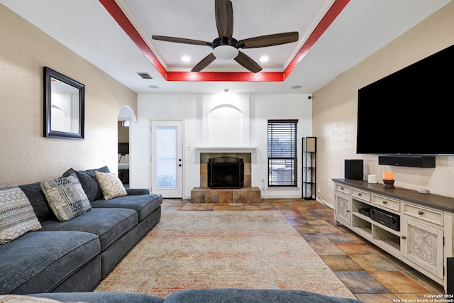 living room featuring ceiling fan, a tray ceiling, crown molding, and a tile fireplace