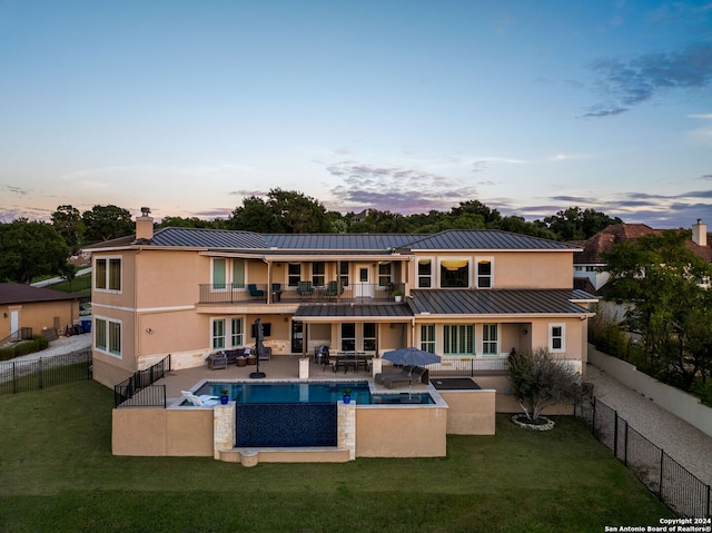 back house at dusk with a lawn, a balcony, outdoor lounge area, and a patio area