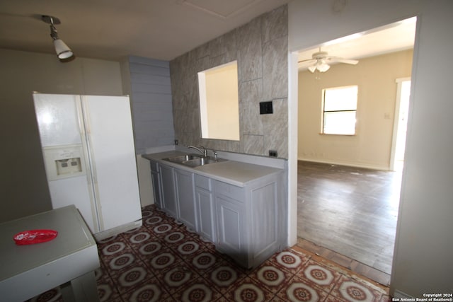 kitchen with tile walls, wood-type flooring, ceiling fan, white fridge with ice dispenser, and sink