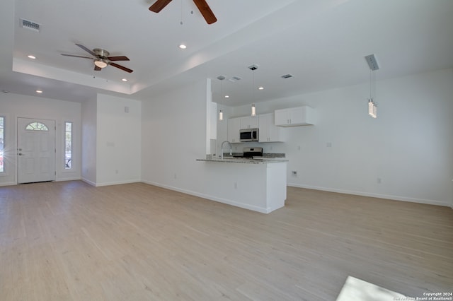 unfurnished living room featuring light wood-type flooring, a raised ceiling, and ceiling fan