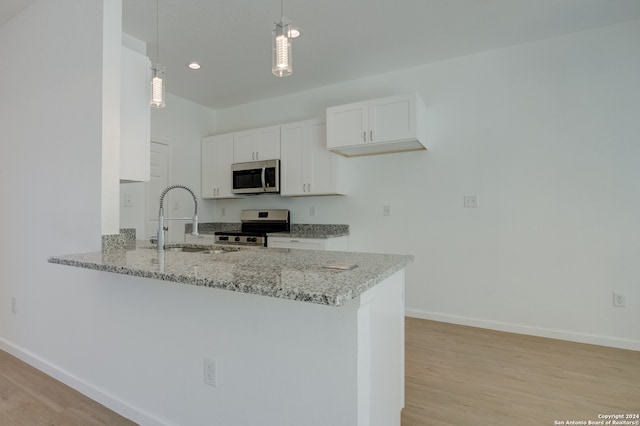 kitchen with appliances with stainless steel finishes, white cabinetry, kitchen peninsula, pendant lighting, and light hardwood / wood-style flooring