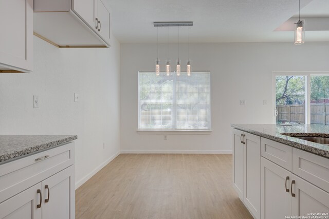 kitchen with white cabinets, light hardwood / wood-style flooring, light stone counters, and decorative light fixtures