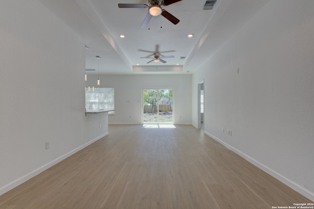 unfurnished living room featuring ceiling fan, a tray ceiling, and light hardwood / wood-style flooring