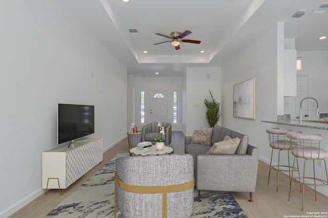 living room with light hardwood / wood-style flooring, ceiling fan, a raised ceiling, and sink