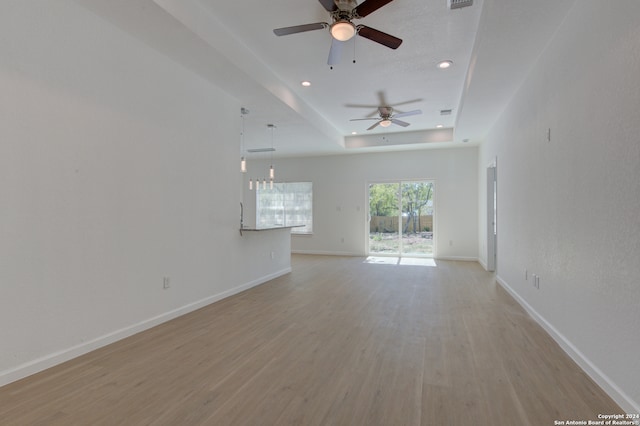 unfurnished living room featuring a tray ceiling, light hardwood / wood-style floors, and ceiling fan