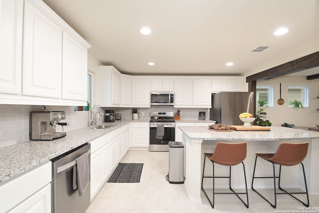 kitchen with light stone counters, stainless steel appliances, a center island, and white cabinetry