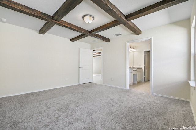 unfurnished bedroom with beam ceiling, ensuite bath, coffered ceiling, and light colored carpet