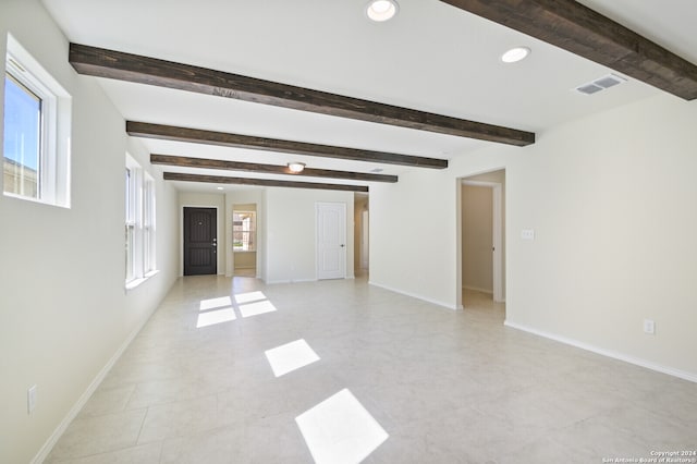 empty room with a healthy amount of sunlight, beam ceiling, and light tile patterned floors