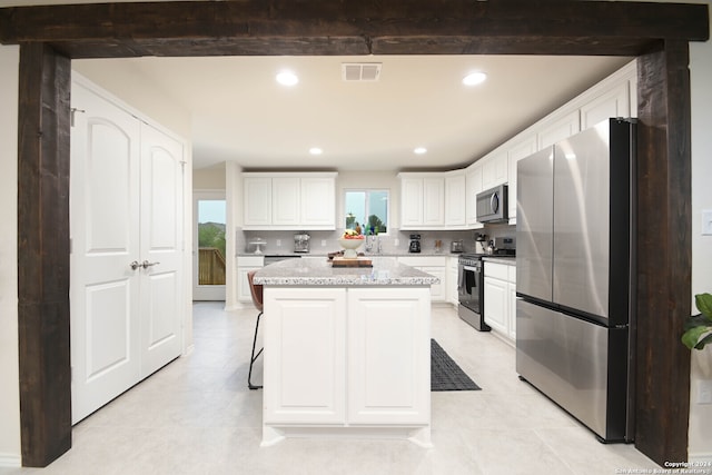 kitchen featuring a kitchen island, light stone countertops, stainless steel appliances, and white cabinetry