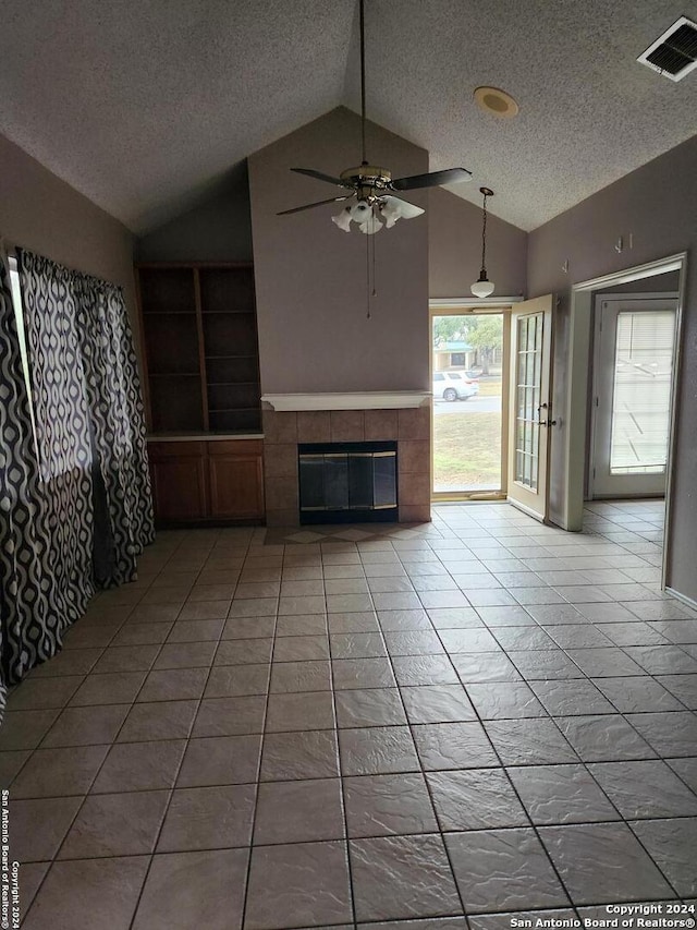 unfurnished living room with ceiling fan, tile patterned flooring, a textured ceiling, vaulted ceiling, and a tiled fireplace