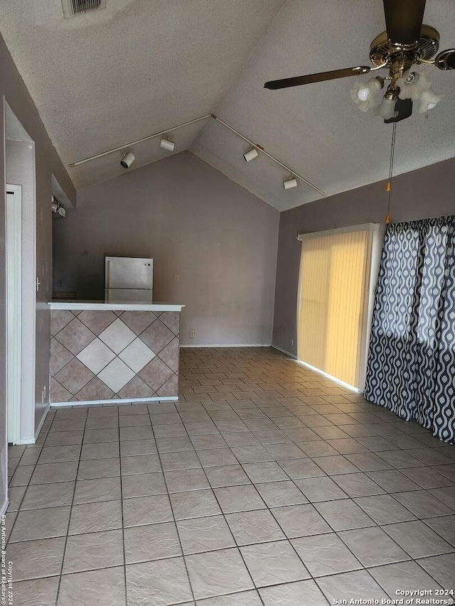 tiled spare room featuring vaulted ceiling, track lighting, ceiling fan, and a textured ceiling