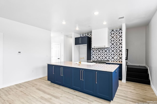 kitchen with a center island with sink, blue cabinets, sink, and light hardwood / wood-style floors