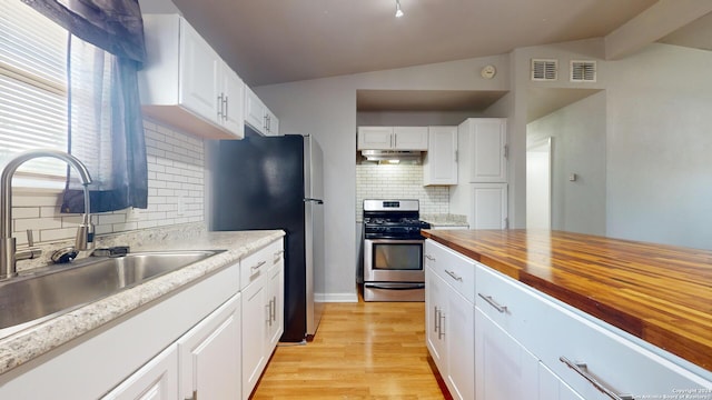 kitchen featuring white cabinetry, backsplash, stainless steel appliances, wooden counters, and lofted ceiling