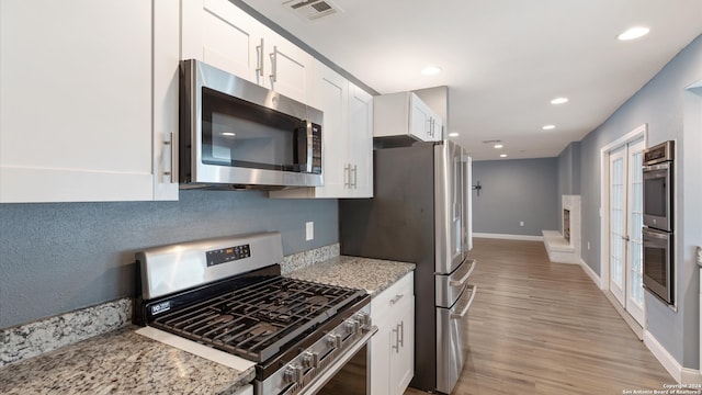 kitchen featuring light stone countertops, stainless steel appliances, white cabinets, and light hardwood / wood-style floors