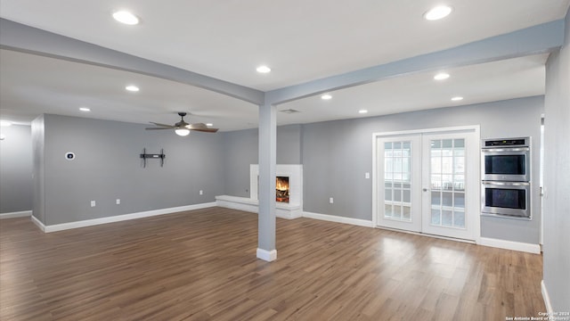 unfurnished living room featuring hardwood / wood-style floors, ceiling fan, french doors, and a brick fireplace