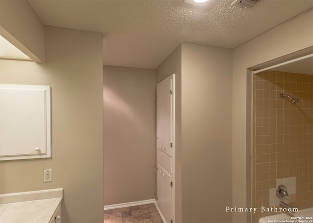 bathroom featuring a textured ceiling, tiled shower, and vanity