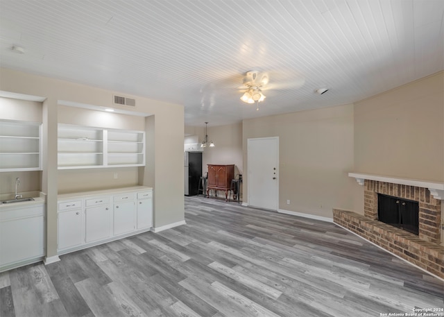 unfurnished living room with ceiling fan, built in shelves, sink, a fireplace, and light wood-type flooring