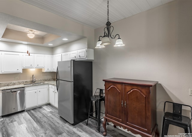 kitchen with pendant lighting, white cabinets, a raised ceiling, sink, and appliances with stainless steel finishes