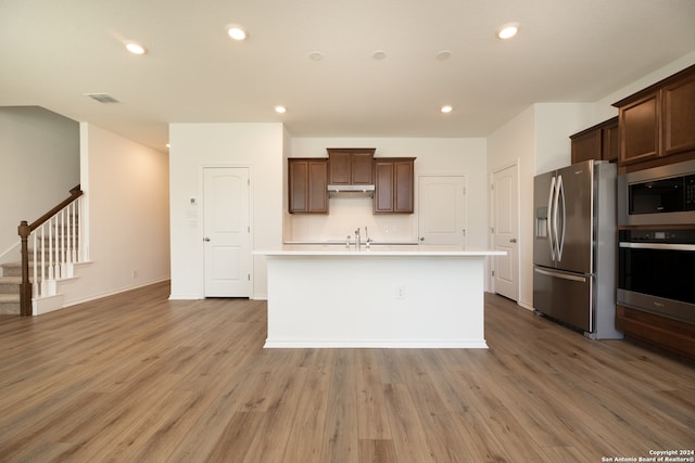 kitchen with an island with sink, appliances with stainless steel finishes, and light wood-type flooring