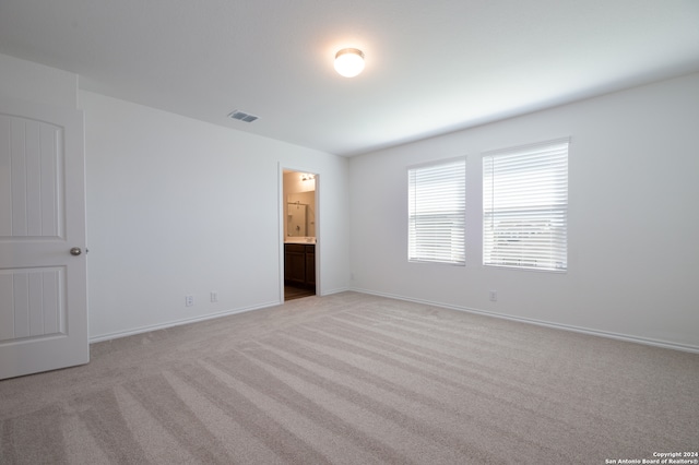 unfurnished bedroom featuring light carpet and ensuite bath