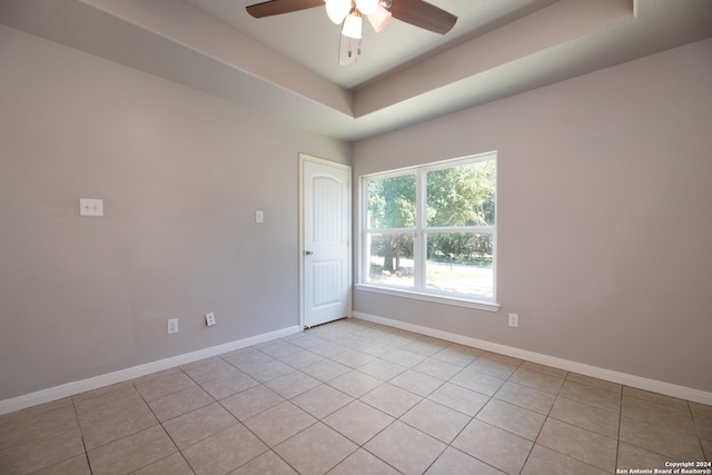 empty room featuring ceiling fan, a raised ceiling, and light tile patterned floors