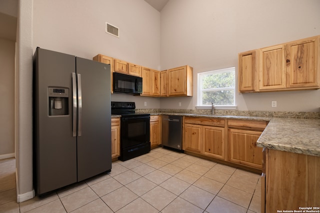 kitchen featuring a high ceiling, black appliances, light tile patterned floors, and sink