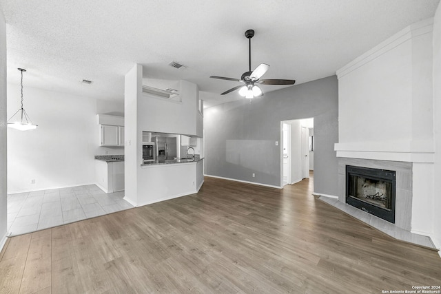 unfurnished living room with sink, light hardwood / wood-style flooring, ceiling fan, a textured ceiling, and a large fireplace