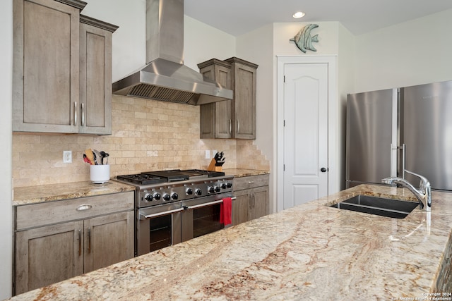 kitchen featuring light stone counters, sink, premium appliances, backsplash, and wall chimney range hood