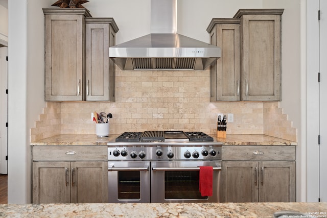 kitchen featuring range with two ovens, light stone counters, wall chimney range hood, and tasteful backsplash