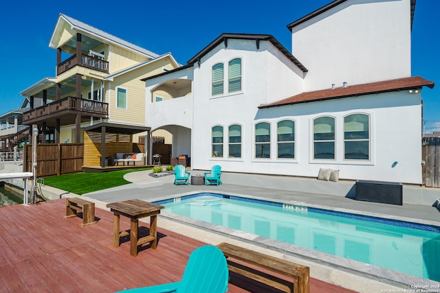 back of property with a balcony, an outdoor living space, a swimming pool with hot tub, and a patio area