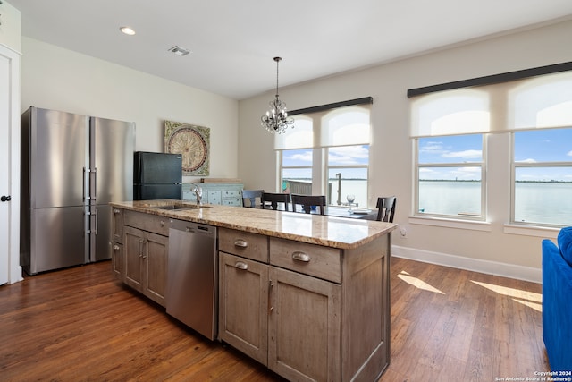 kitchen featuring appliances with stainless steel finishes, hanging light fixtures, dark wood-type flooring, light stone countertops, and a center island with sink