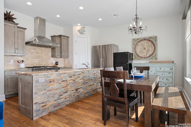 kitchen with light stone counters, wall chimney range hood, high quality fridge, hardwood / wood-style floors, and black fridge