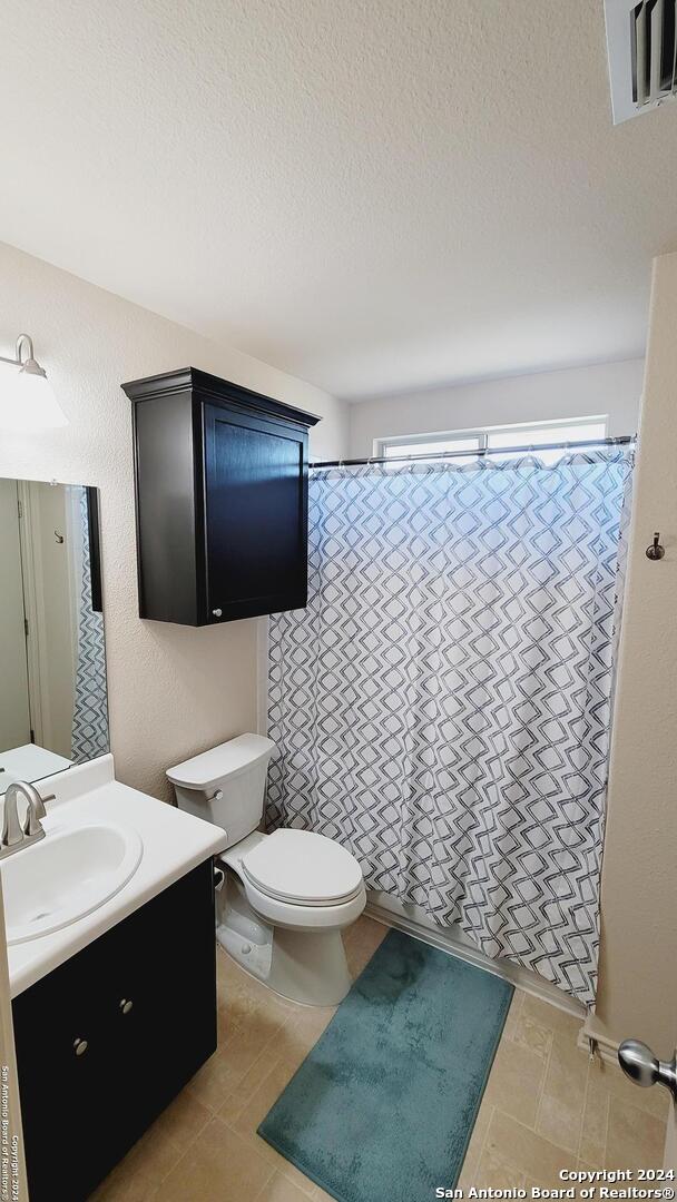 bathroom with walk in shower, a textured ceiling, vanity, and toilet