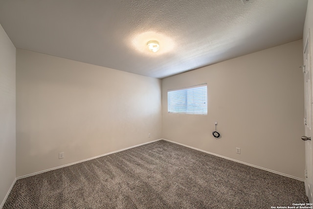 spare room featuring a textured ceiling and dark colored carpet