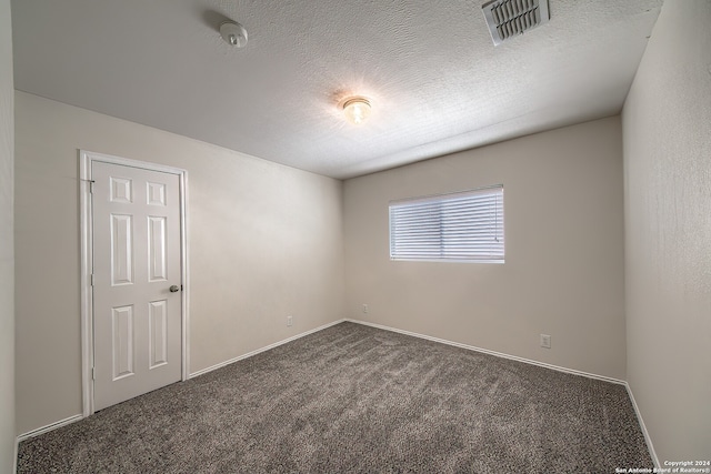 empty room featuring dark carpet and a textured ceiling