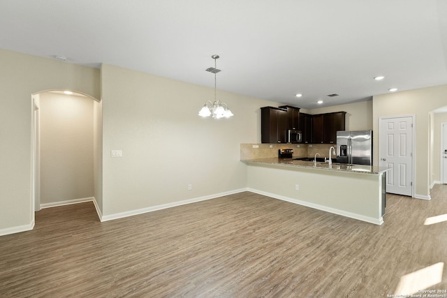 kitchen with appliances with stainless steel finishes, kitchen peninsula, dark brown cabinets, light hardwood / wood-style flooring, and decorative light fixtures