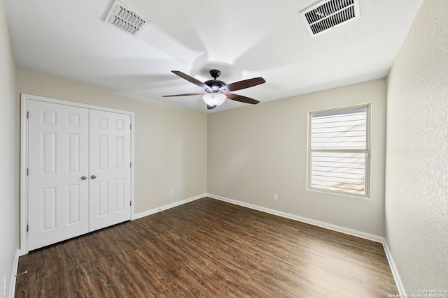 unfurnished bedroom with ceiling fan, a textured ceiling, a closet, and dark hardwood / wood-style floors