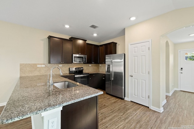 kitchen with light hardwood / wood-style floors, light stone counters, kitchen peninsula, stainless steel appliances, and sink