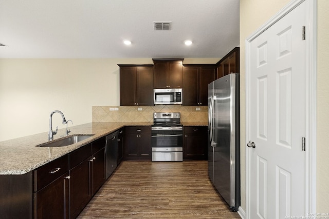 kitchen with light stone counters, sink, kitchen peninsula, stainless steel appliances, and dark hardwood / wood-style flooring