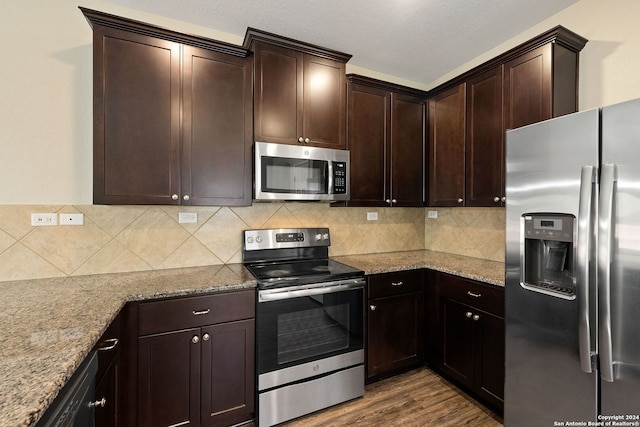 kitchen with light stone counters, backsplash, stainless steel appliances, dark brown cabinetry, and dark hardwood / wood-style floors