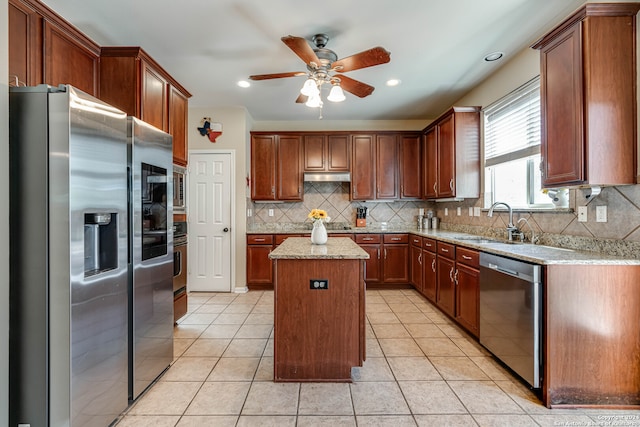 kitchen with sink, a kitchen island, backsplash, stainless steel appliances, and light stone countertops