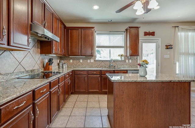 kitchen featuring black electric stovetop, a center island, sink, backsplash, and light stone countertops