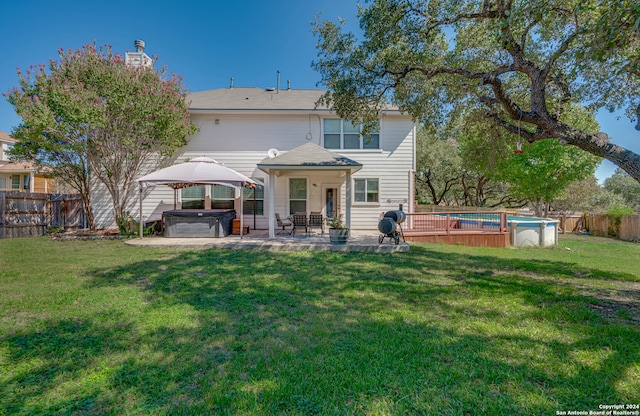 rear view of house featuring a patio, a yard, and a swimming pool with hot tub