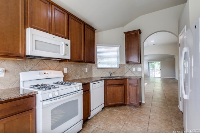 kitchen featuring arched walkways, lofted ceiling, backsplash, a sink, and white appliances