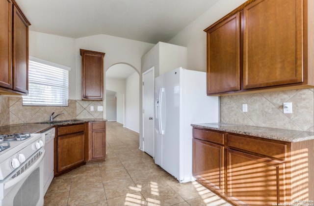 kitchen with brown cabinets, stone counters, white appliances, and a sink