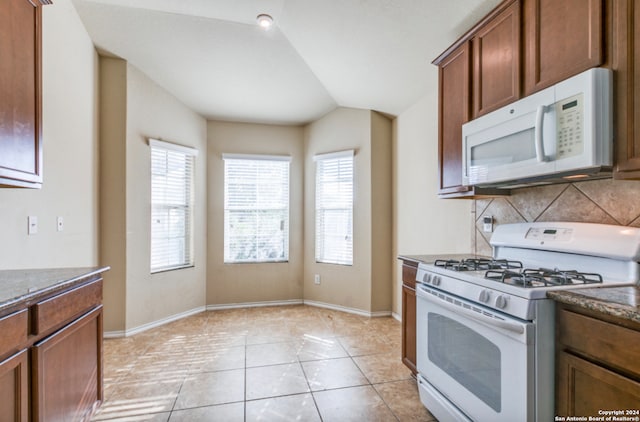 kitchen with lofted ceiling, light tile patterned floors, white appliances, tasteful backsplash, and dark countertops